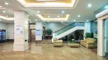 A hotel lobby with a marble floor, a staircase, and seating areas.