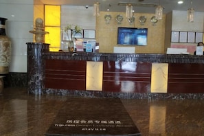 A reception desk with a marble top, a digital screen, and a decorative vase.