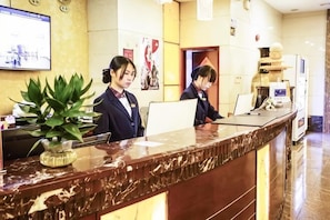 A reception desk with two staff members, a potted plant, and a coffee machine. - Dong Chang Hotel (Dongguan Hengli China Resources Shopping Plaza) (Dongguan)