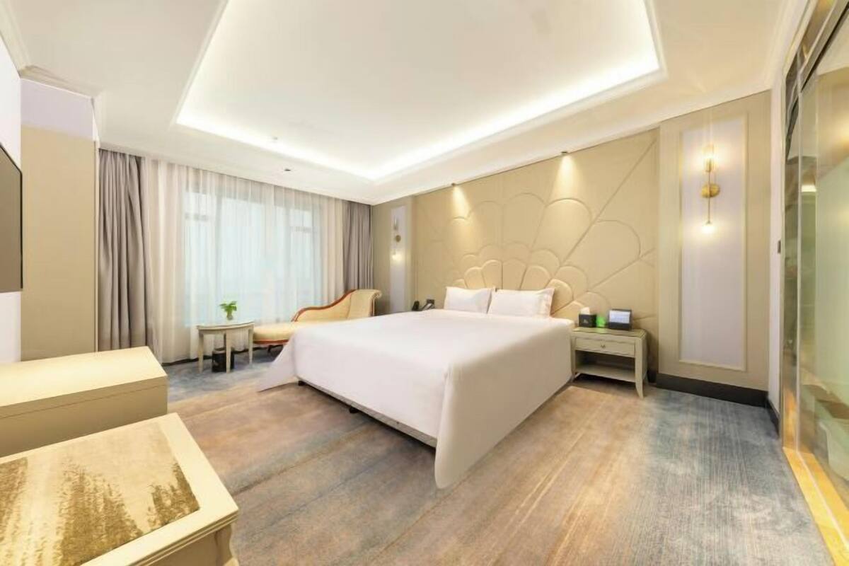 Hotellihuone, jossa on suuri sänky, yöpöydät, pieni pöytä tuolilla sekä suuri ikkuna, jossa on verhot.