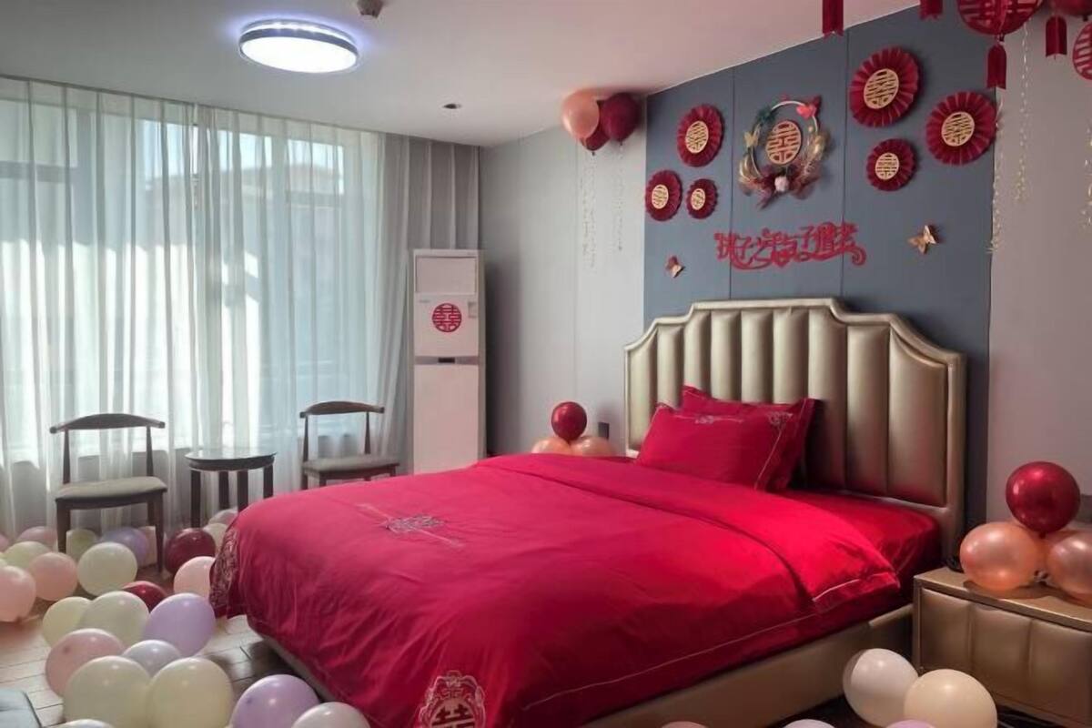 Hotellihuone, jossa on suuri sänky, yöpöytä, tuoli ja ikkuna, jossa on verhot.