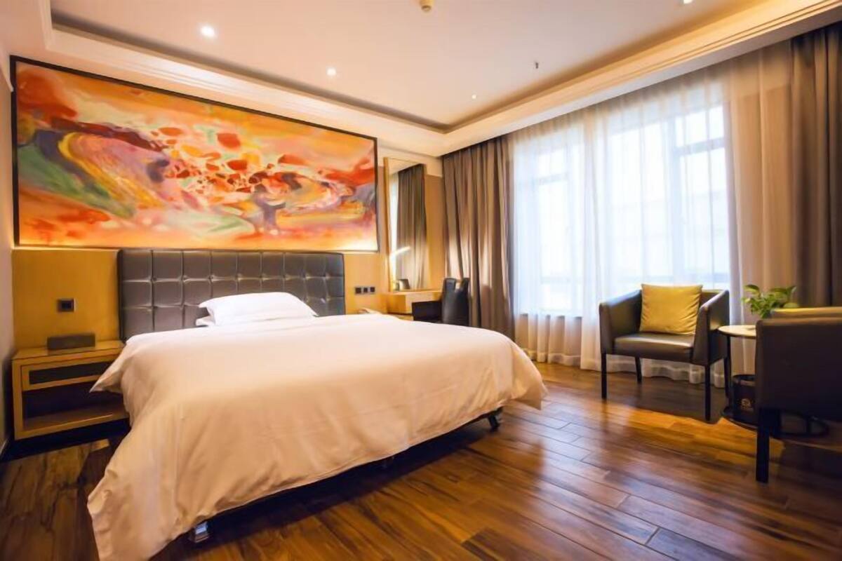Hotellihuone, jossa on suuri sänky, moderni sängynpääty, työpöytä tuolilla ja suuri abstrakti maalaus seinällä.