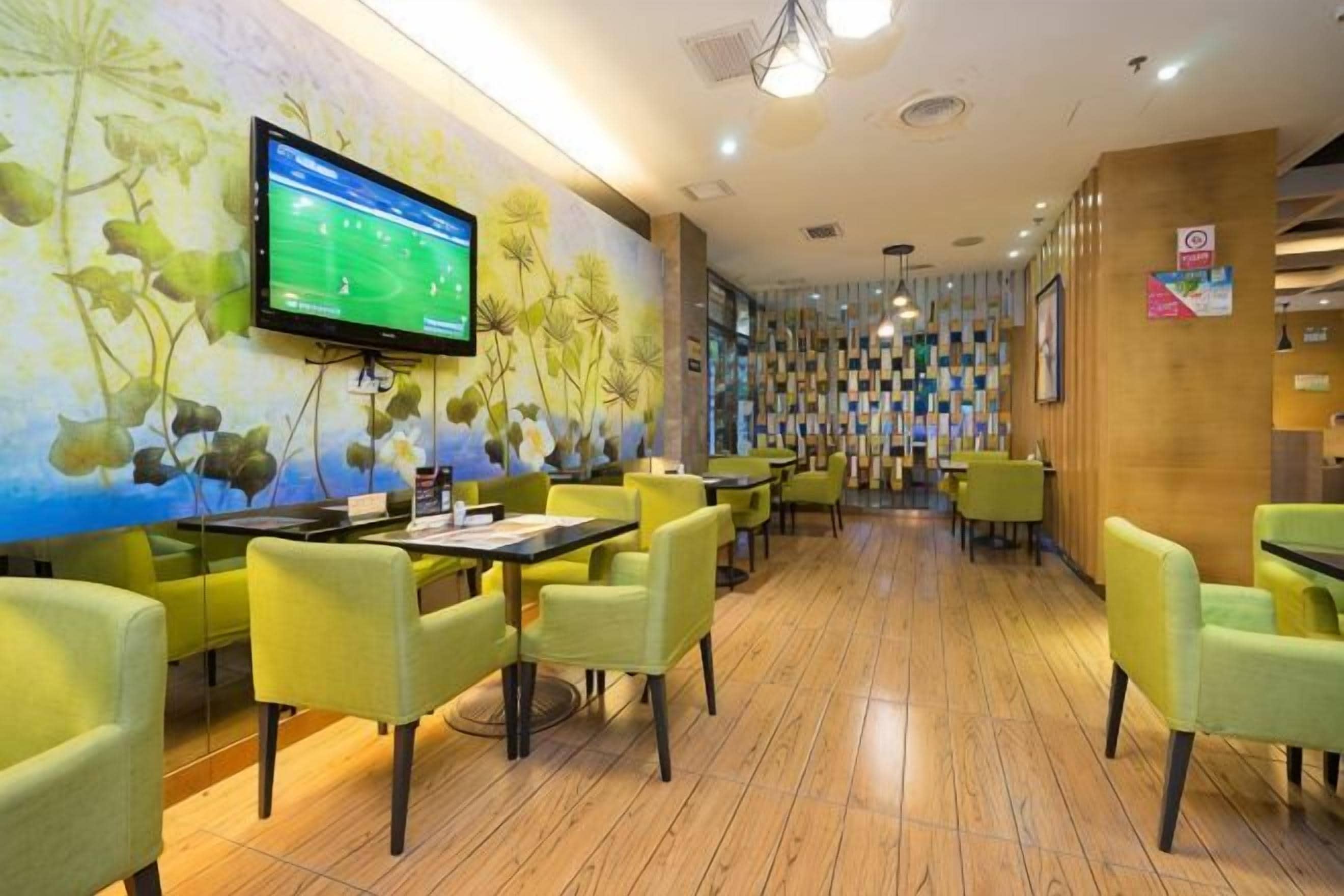 A restaurant with tables and chairs, a television screen, and a wall with a floral mural.