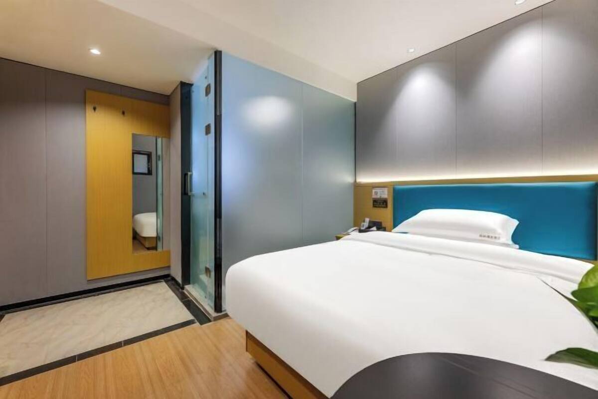 Una habitación de hotel moderna con una cama grande, una mesita de noche, un espejo y suelo de madera.
