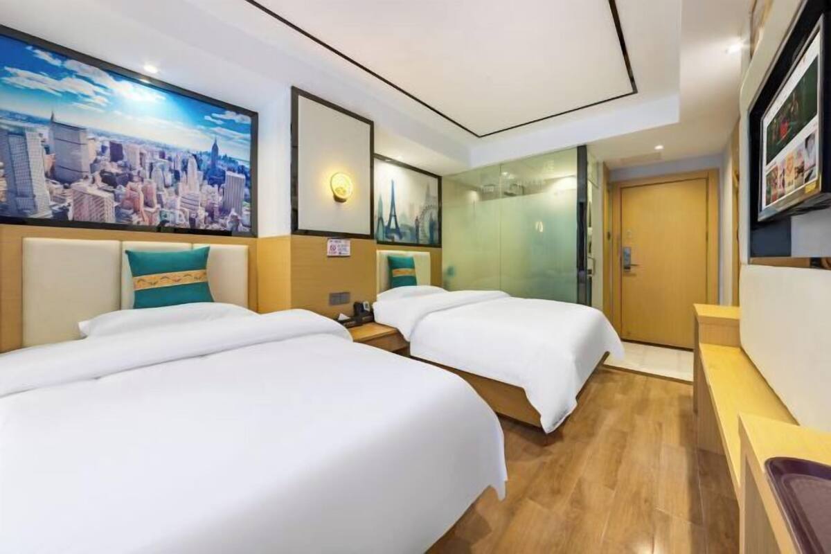 Habitación de hotel con dos camas, un cuadro de paisaje urbano, cabina de ducha de vidrio y suelo de madera.