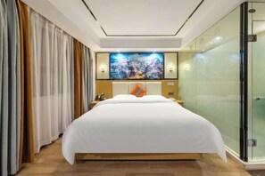 A hotel room with a large bed, a glass partition, and a wall-mounted TV.