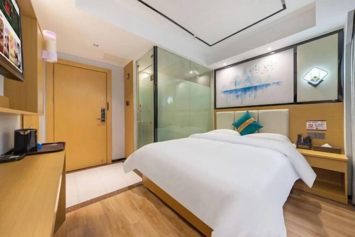 Una habitación de hotel con cama, escritorio, separador de vidrio y una obra de arte colgada en la pared.