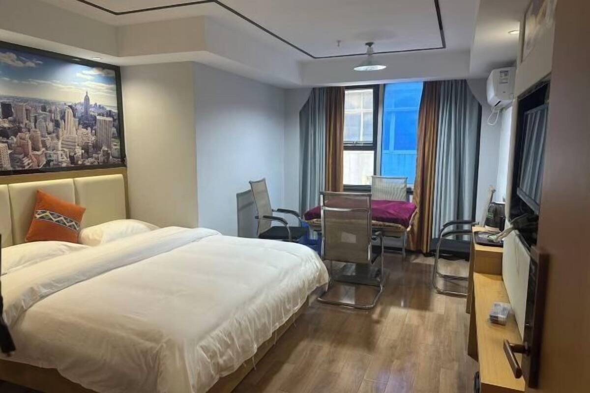 Habitación de hotel con una cama grande, un escritorio, una silla, un televisor y una ventana con cortinas.