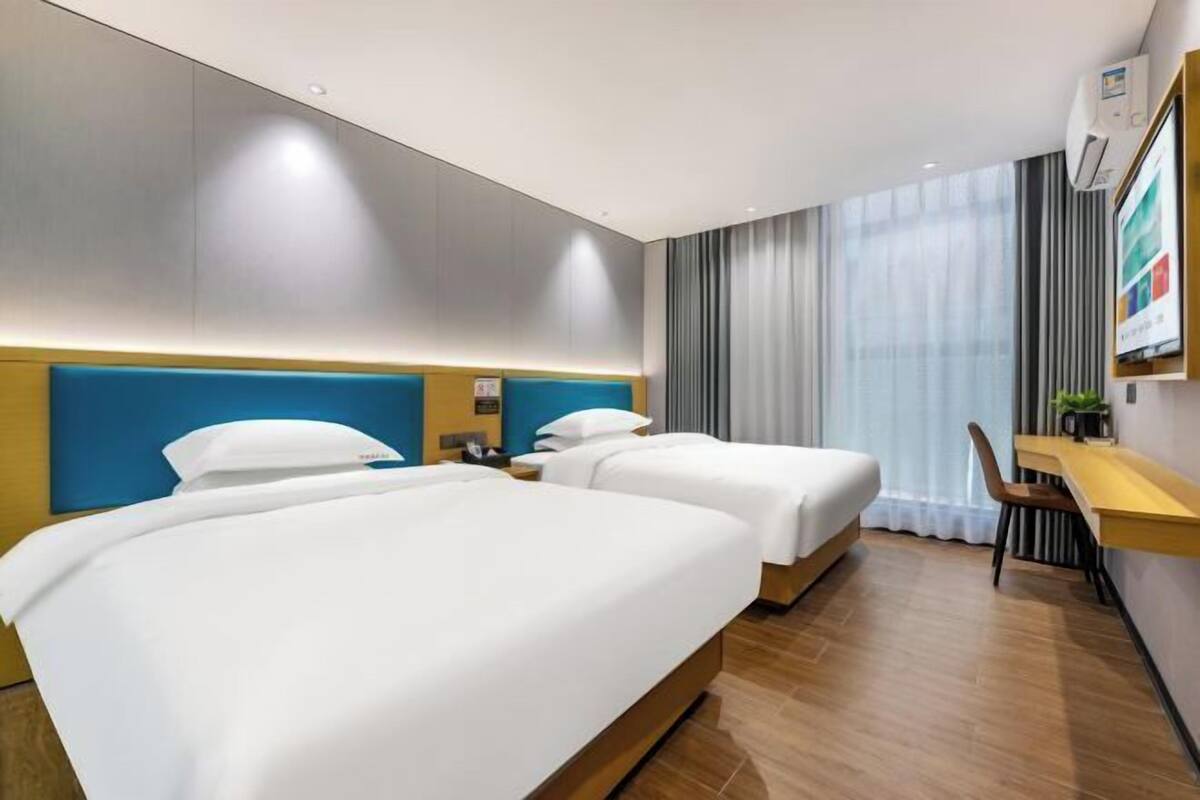 Habitación de hotel con dos camas, un escritorio y un ventanal grande con cortinas.