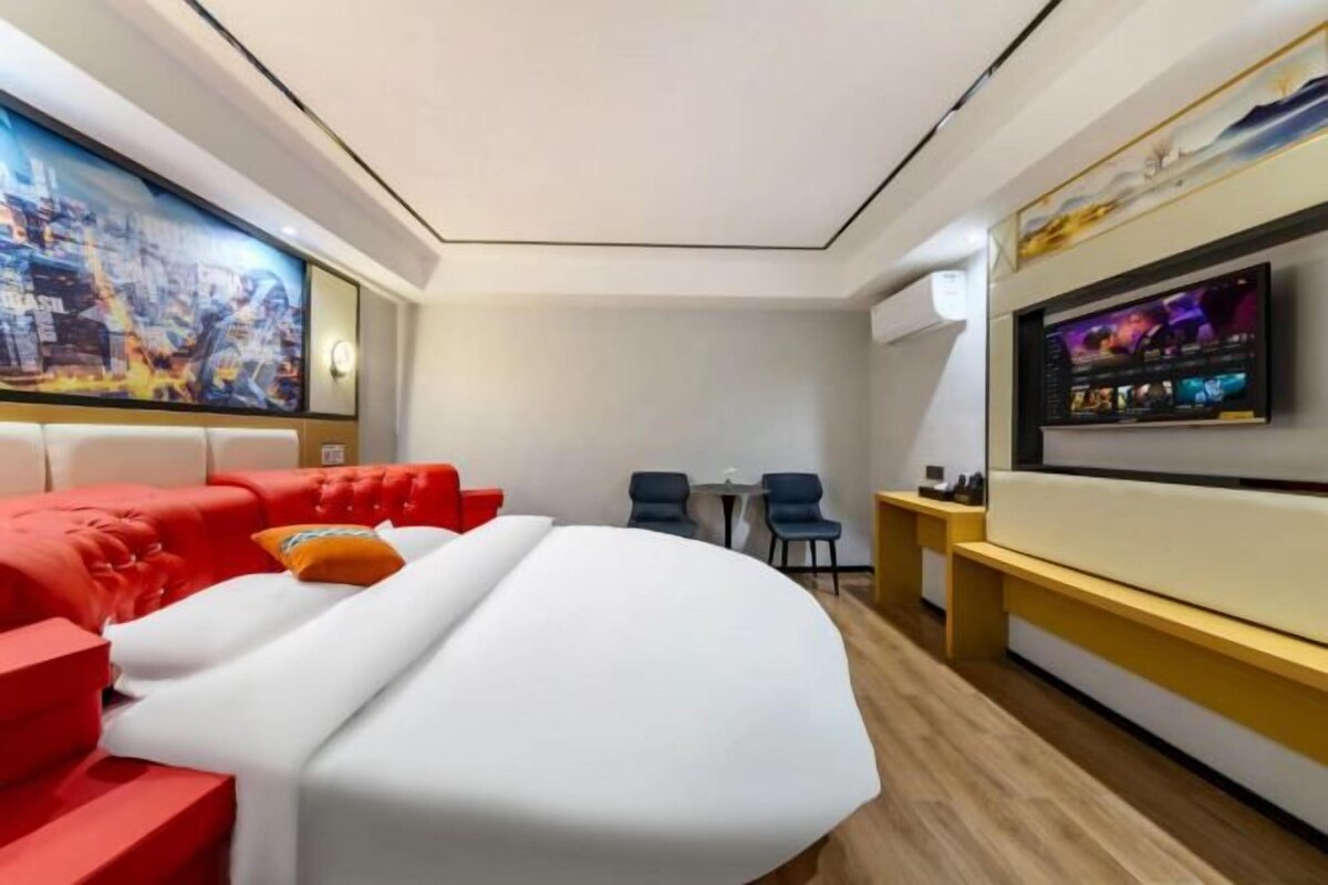 A modern hotel room with a large bed, a TV mounted on the wall, and a cityscape painting above the bed.