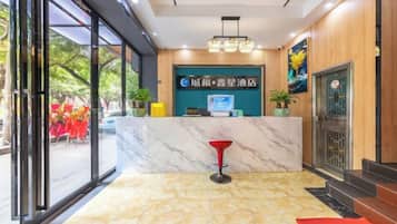 A hotel reception area with a marble counter, a red bar stool, and a digital screen displaying the hotel name.