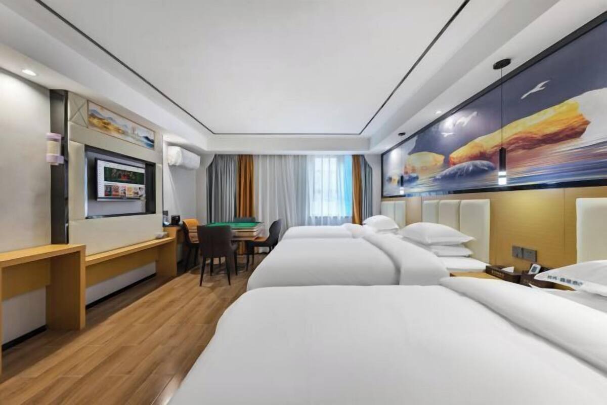 Una habitación de hotel con escritorio, dos camas, un cuadro en la pared y una ventana con cortinas.