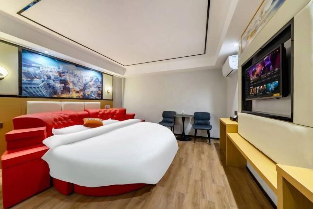 Una habitación de hotel moderna con una cama grande, una zona de estar roja, un televisor y un mural con vista a la ciudad.