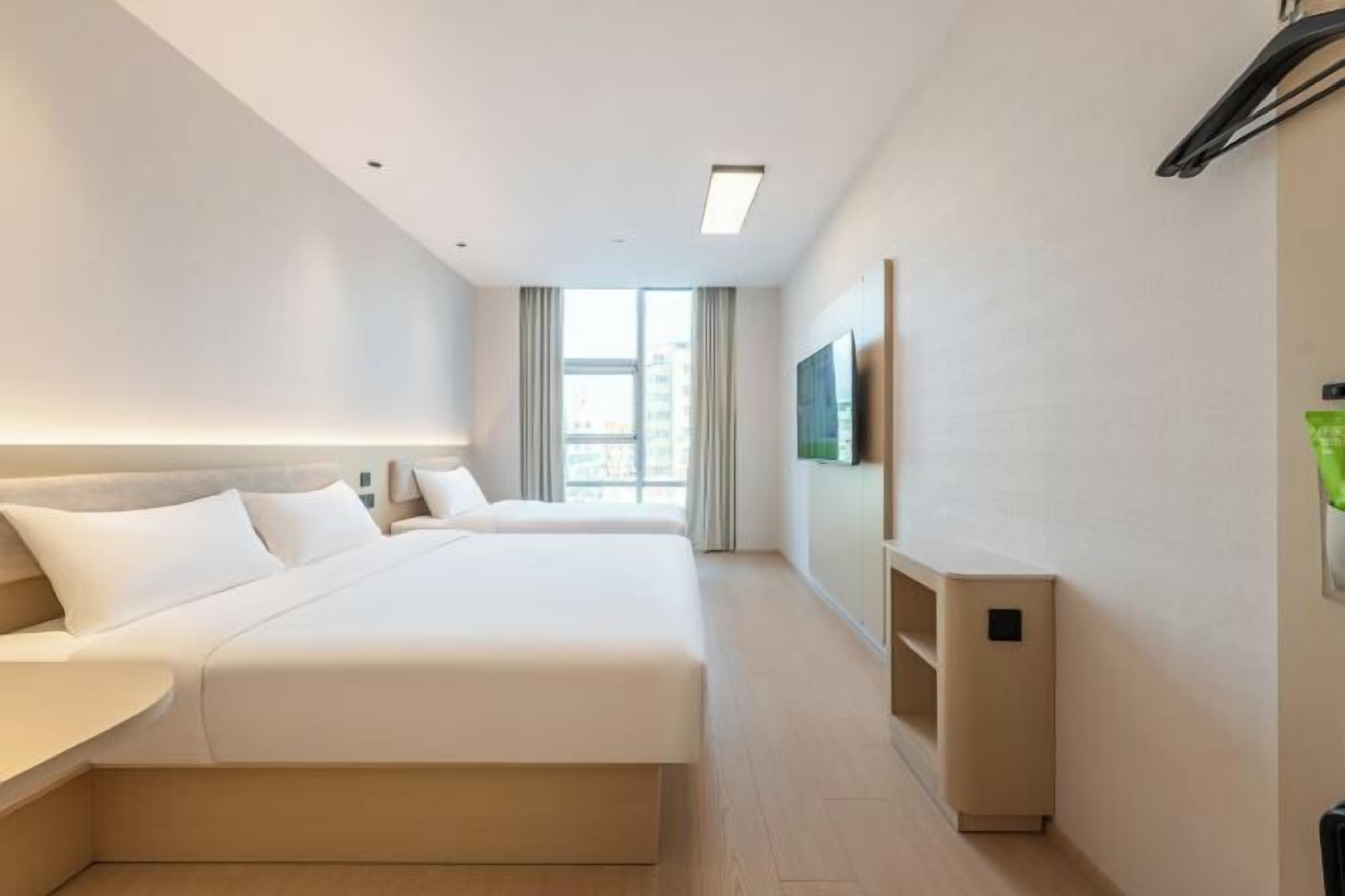 A hotel room with a large bed, a bedside table, a TV mounted on the wall, and a window with curtains.