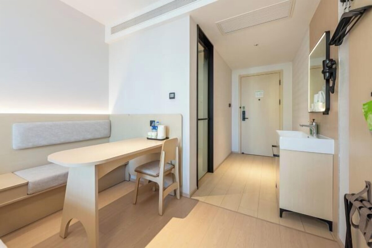 Ein modernes Hotelzimmer im minimalistischen Stil mit Sofa, Schreibtisch und einem Badezimmer mit Waschbecken und Spiegel.