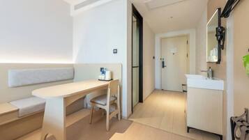 Habitación de hotel moderna con diseño minimalista, que incluye un sofá, un escritorio y un baño con lavabo y espejo.