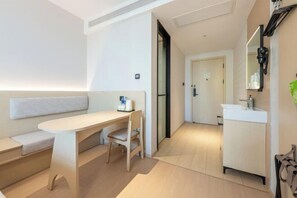 Ein modernes Hotelzimmer im minimalistischen Stil mit Sofa, Schreibtisch und einem Badezimmer mit Waschbecken und Spiegel.