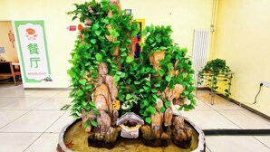 A reception area with a decorative plant arrangement, a sign for a restaurant, and a radiator on the wall. - Days Inn Chain Hotel (Beijing Shangdi Xixiaokou Subway Station) (Beijing)