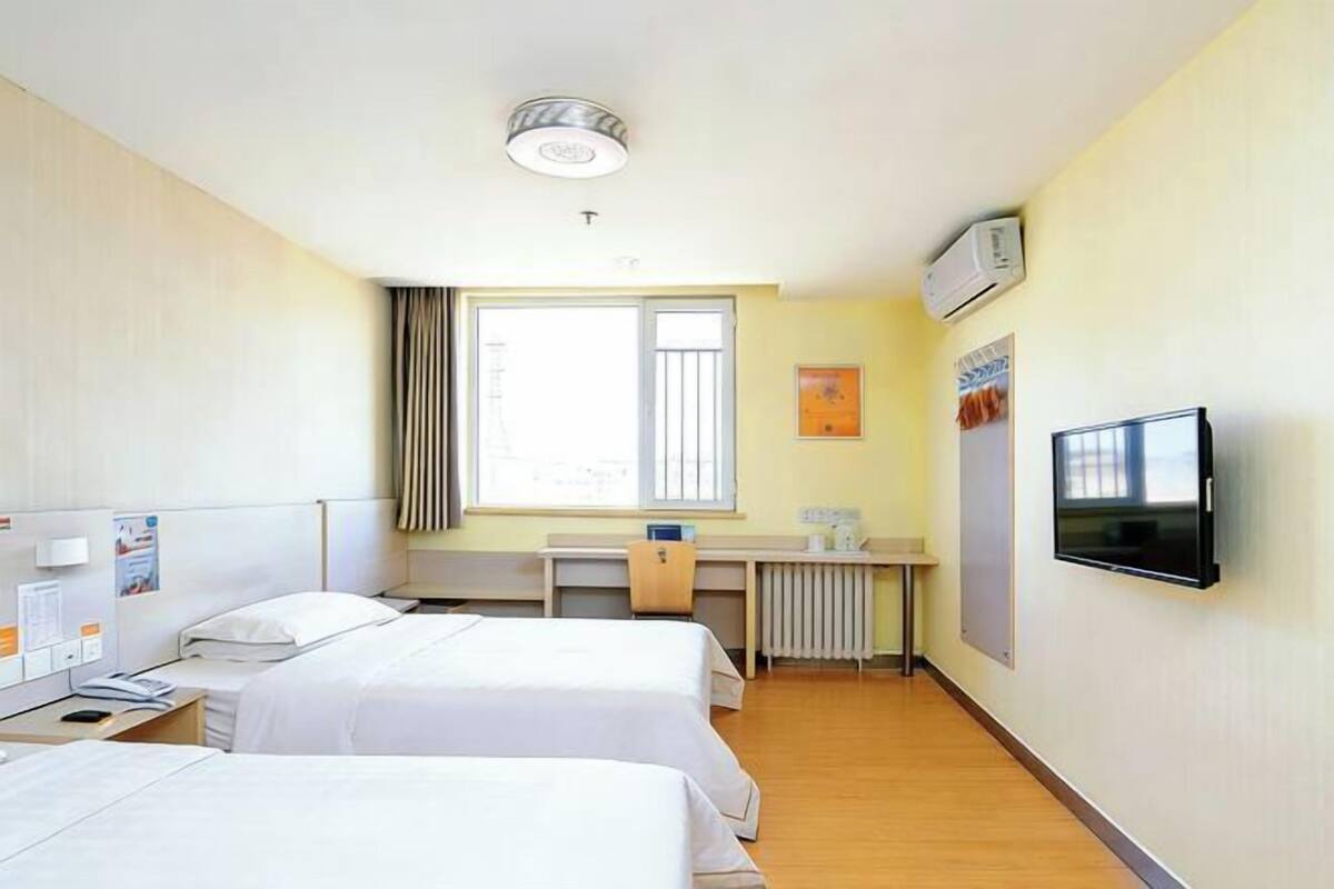 Une chambre d’hôtel avec deux lits, un bureau, une chaise, une télévision et une fenêtre avec des rideaux.
