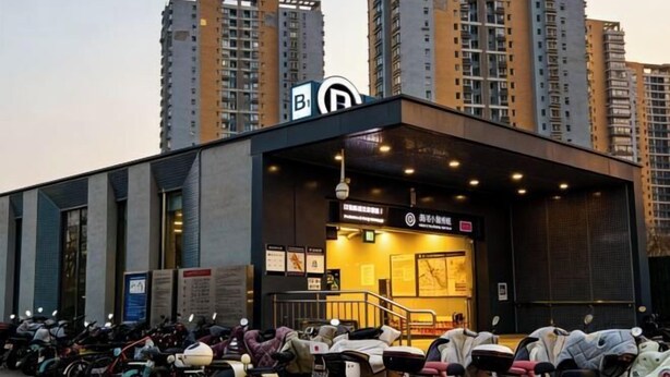 A building with a sign indicating a parking area for bicycles and scooters, surrounded by tall residential buildings. - Days Inn Chain Hotel (Beijing Shangdi Xixiaokou Subway Station) (Beijing)