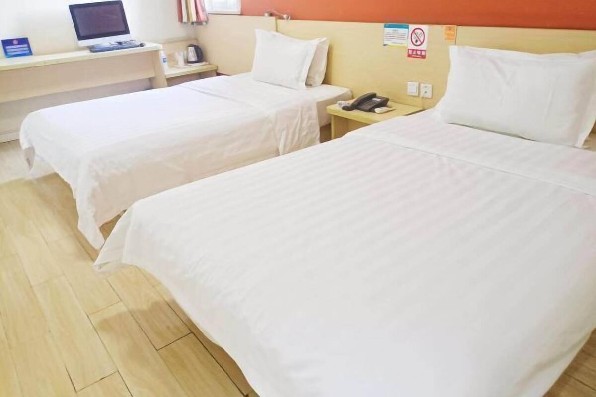 Une chambre d’hôtel avec deux lits, un bureau avec un ordinateur, un téléphone et un panneau fixé au mur.