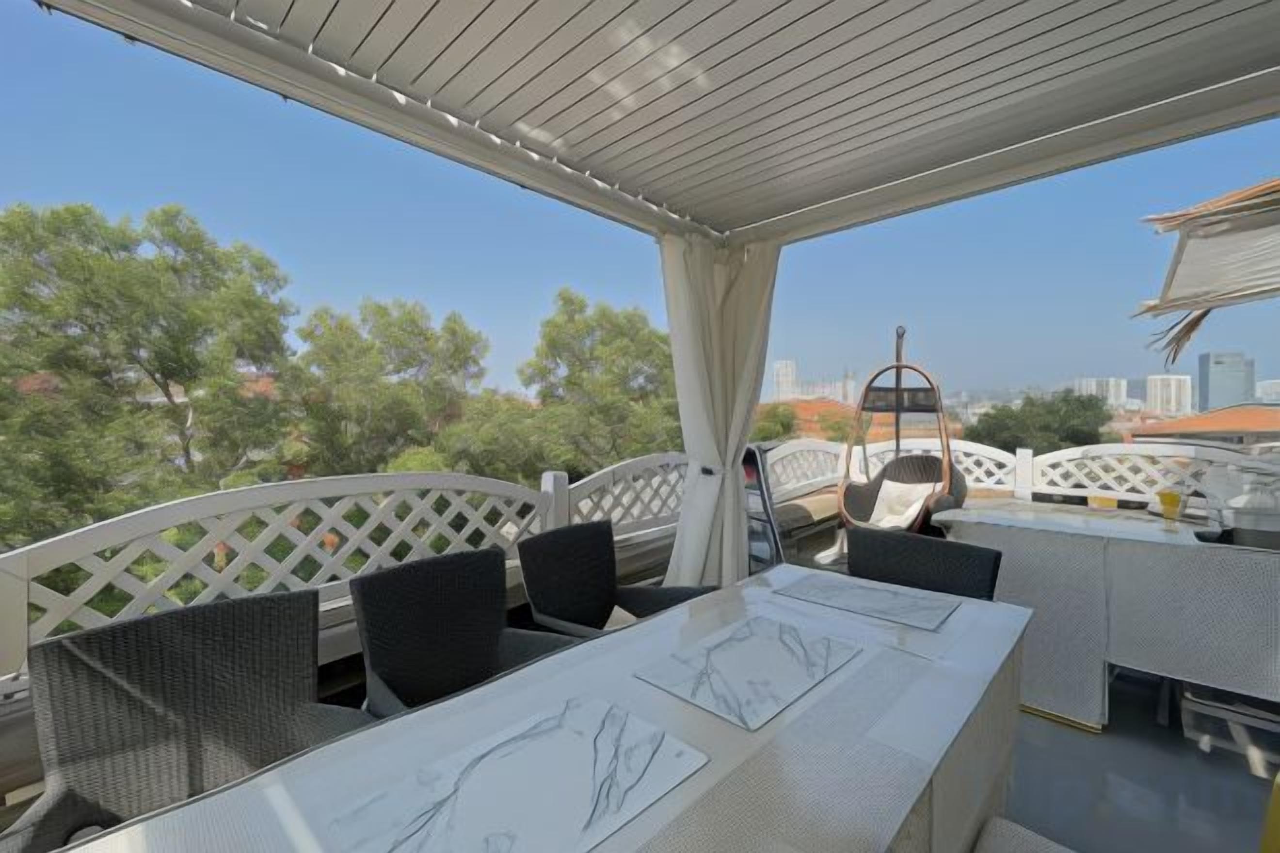 An outdoor patio with a table and chairs, a pergola, and a view of trees and buildings.