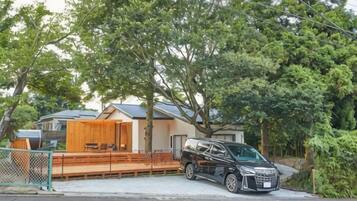 A black car parked in front of a house with a covered outdoor seating area.