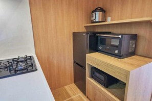 A compact kitchen with a gas stove, a microwave, a refrigerator, and a wooden cabinet. - VOYAN RESORT Izu MADOKA (Ito)