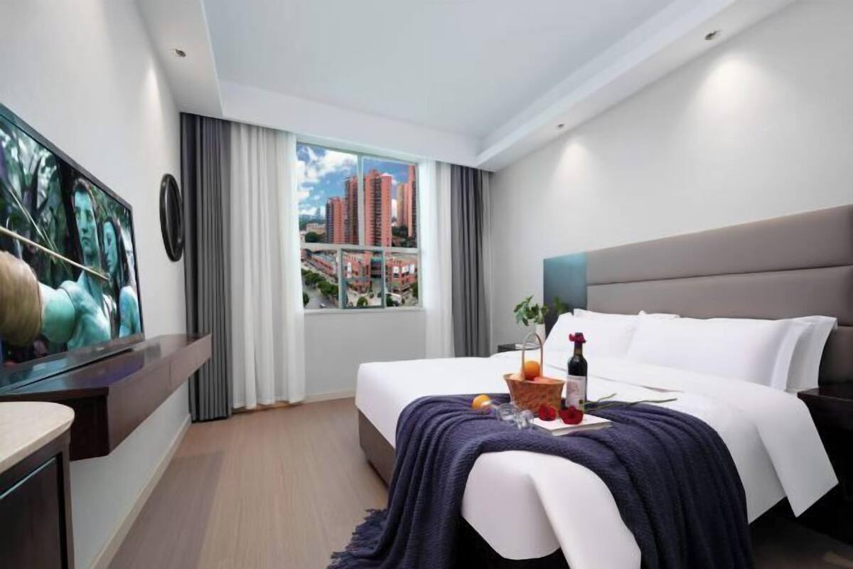 Una moderna camera d'albergo con un ampio letto, una televisione, una finestra con vista sulla città e un vassoio colazione sul letto.