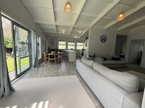 A spacious living area with a large sofa, a dining table, and a kitchen in the background. - Otahu Retreat (Whangamata)