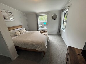 A bedroom with a bed, a window, a mirror, and a small balcony area. - Otahu Retreat (Whangamata)