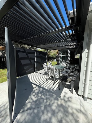 An outdoor patio with a pergola, a table with chairs, and a covered area. - Otahu Retreat (Whangamata)