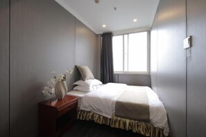 A hotel room with a bed, a nightstand, a vase with flowers, and a window with curtains.