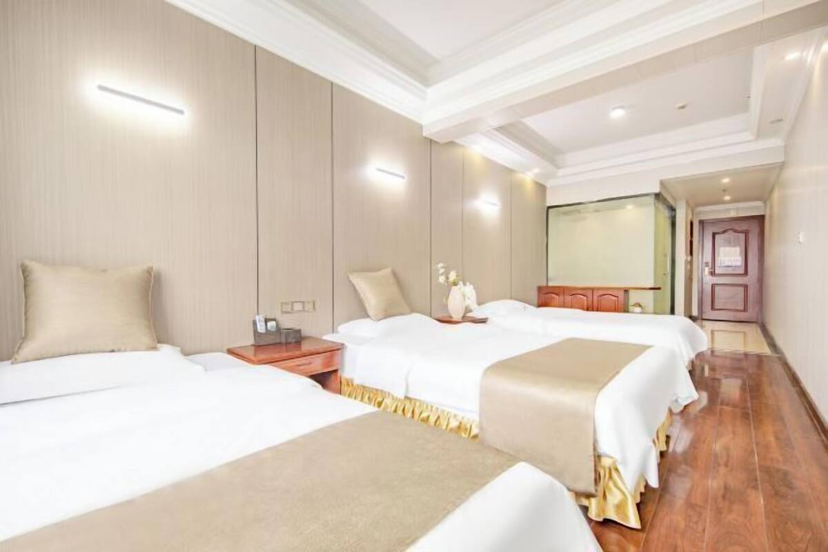 Une chambre d’hôtel avec trois lits, un plancher en bois et un miroir au mur.