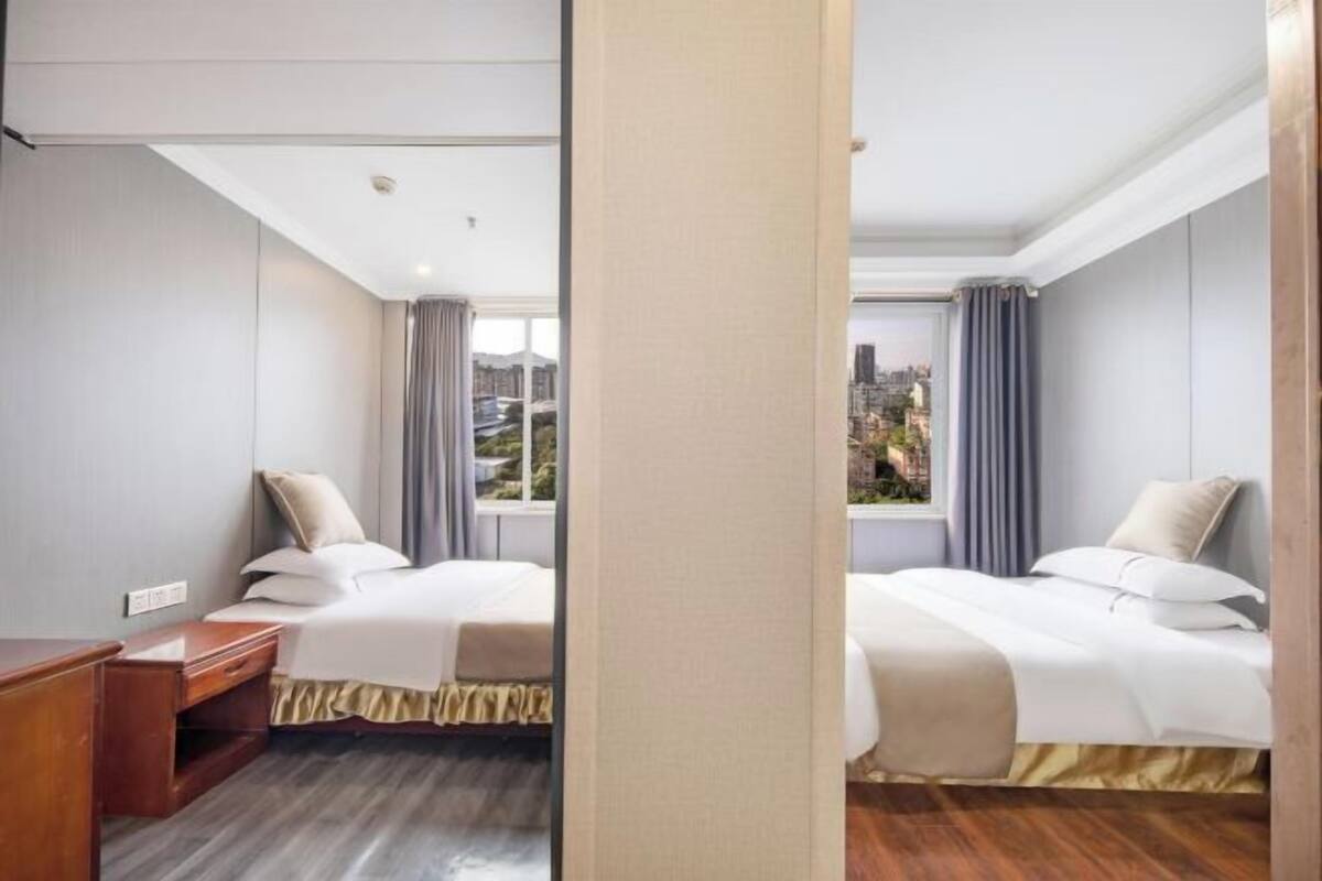 Une chambre d’hôtel avec deux lits, une table de chevet en bois, une fenêtre avec des rideaux et une vue sur des immeubles.