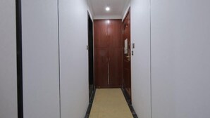 Un couloir étroit, avec une porte en bois au fond, des murs blancs et un sol carrelé.
