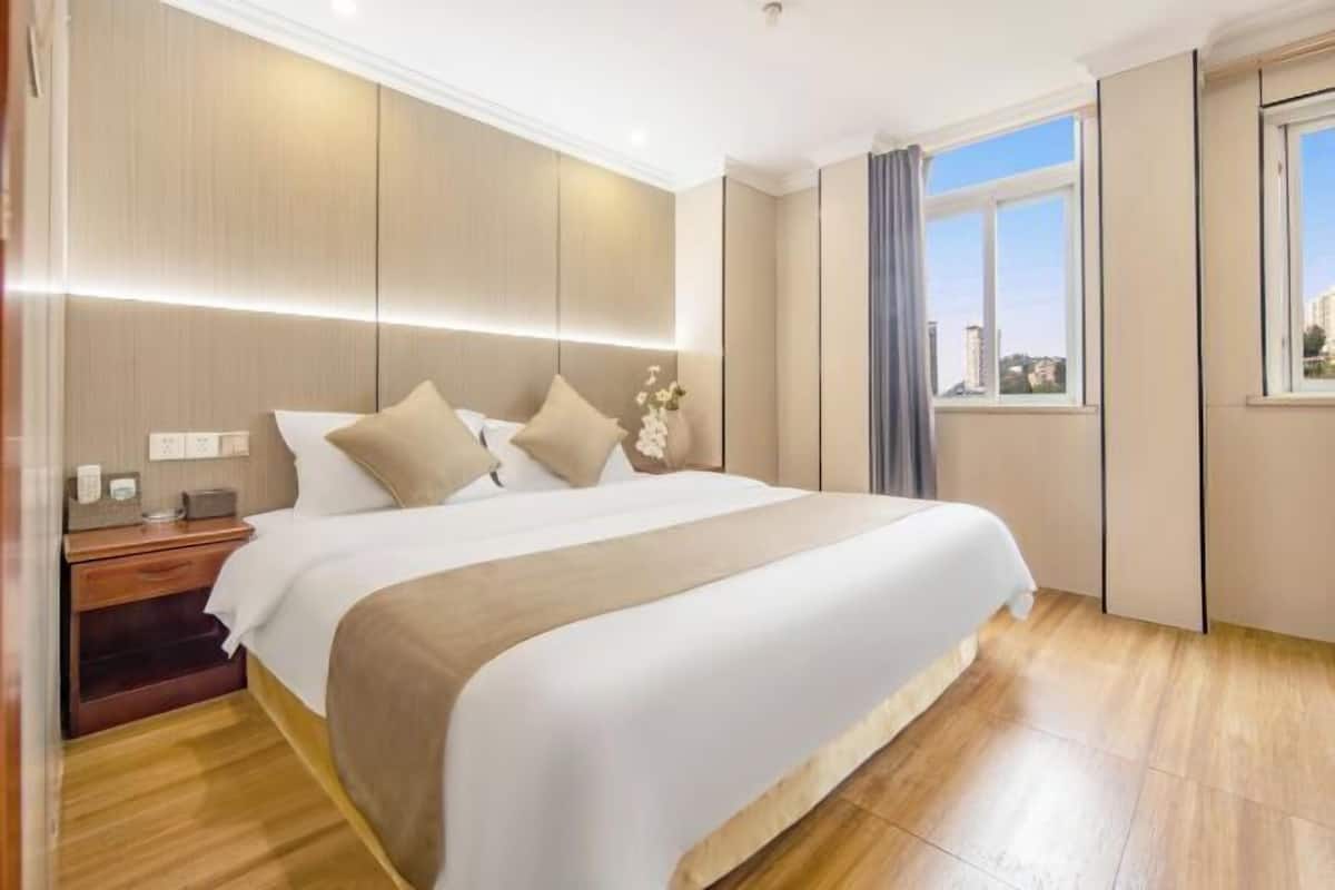 Une chambre d’hôtel moderne dotée d’un grand lit, d’un parquet, d’une table de chevet et d’une fenêtre donnant sur la ville.