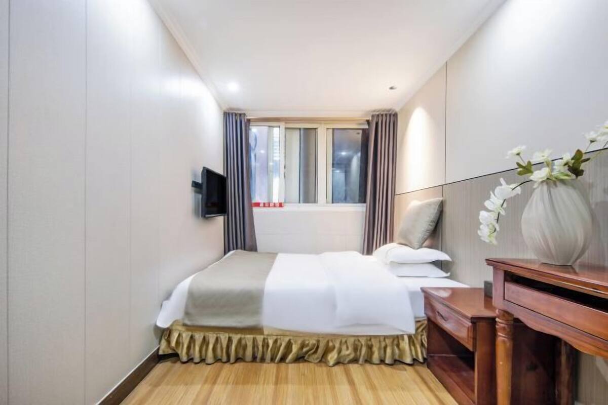 Une chambre d’hôtel avec un lit, un téléviseur fixé au mur, une fenêtre avec des rideaux et un bureau en bois.