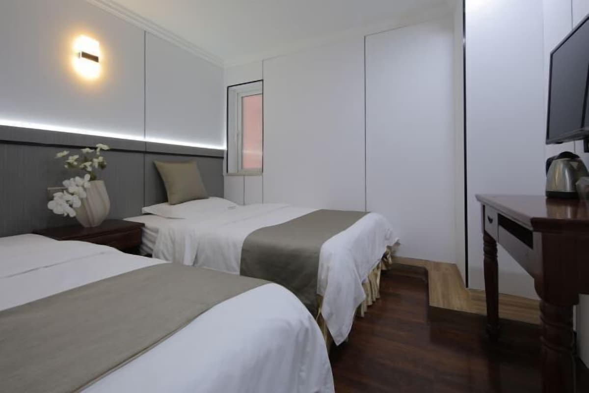 Une chambre d’hôtel avec deux lits, un bureau, une télévision et un luminaire fixé au mur.