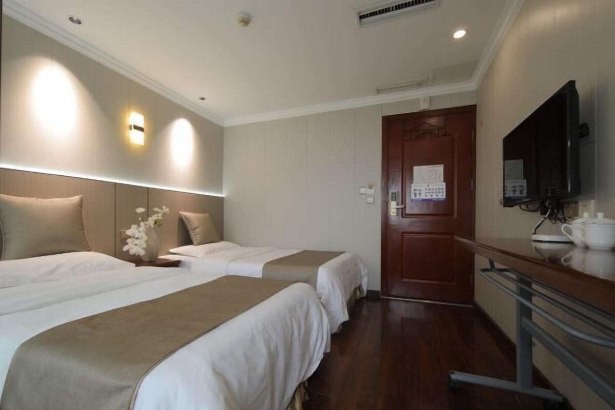 Une chambre d’hôtel avec deux lits, une porte en bois, un téléviseur à écran plat et une petite table avec une théière.