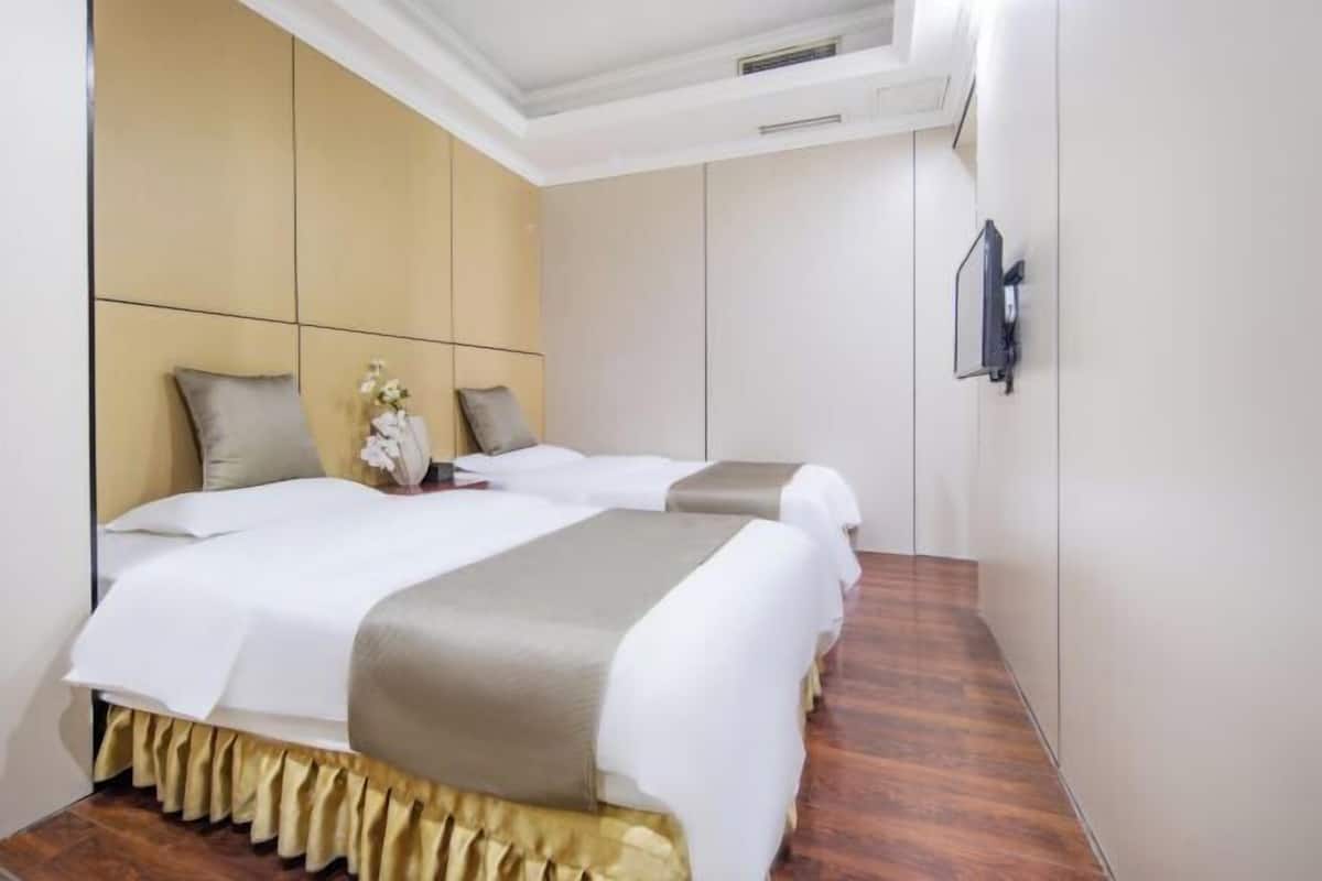 Une chambre d’hôtel avec deux lits, un plancher en bois, un mur blanc et un téléviseur fixé au mur.