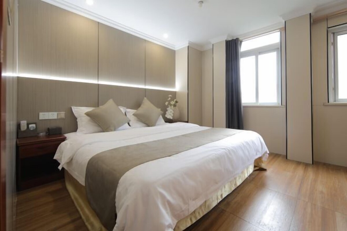 Une chambre d’hôtel moderne avec un grand lit, des tables de chevet, une petite table et une fenêtre avec des rideaux.