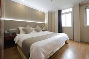 Une chambre d’hôtel moderne avec un grand lit, des tables de chevet, une petite table et une fenêtre avec des rideaux.