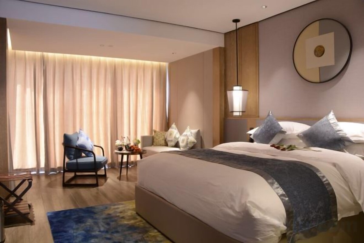 A hotel room with a large bed, a chair, a small table, and a lamp.