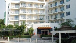 A multi-story hotel with balconies, a covered entrance, and a small garden area. - Shell BAY Resort (Shenzhen)
