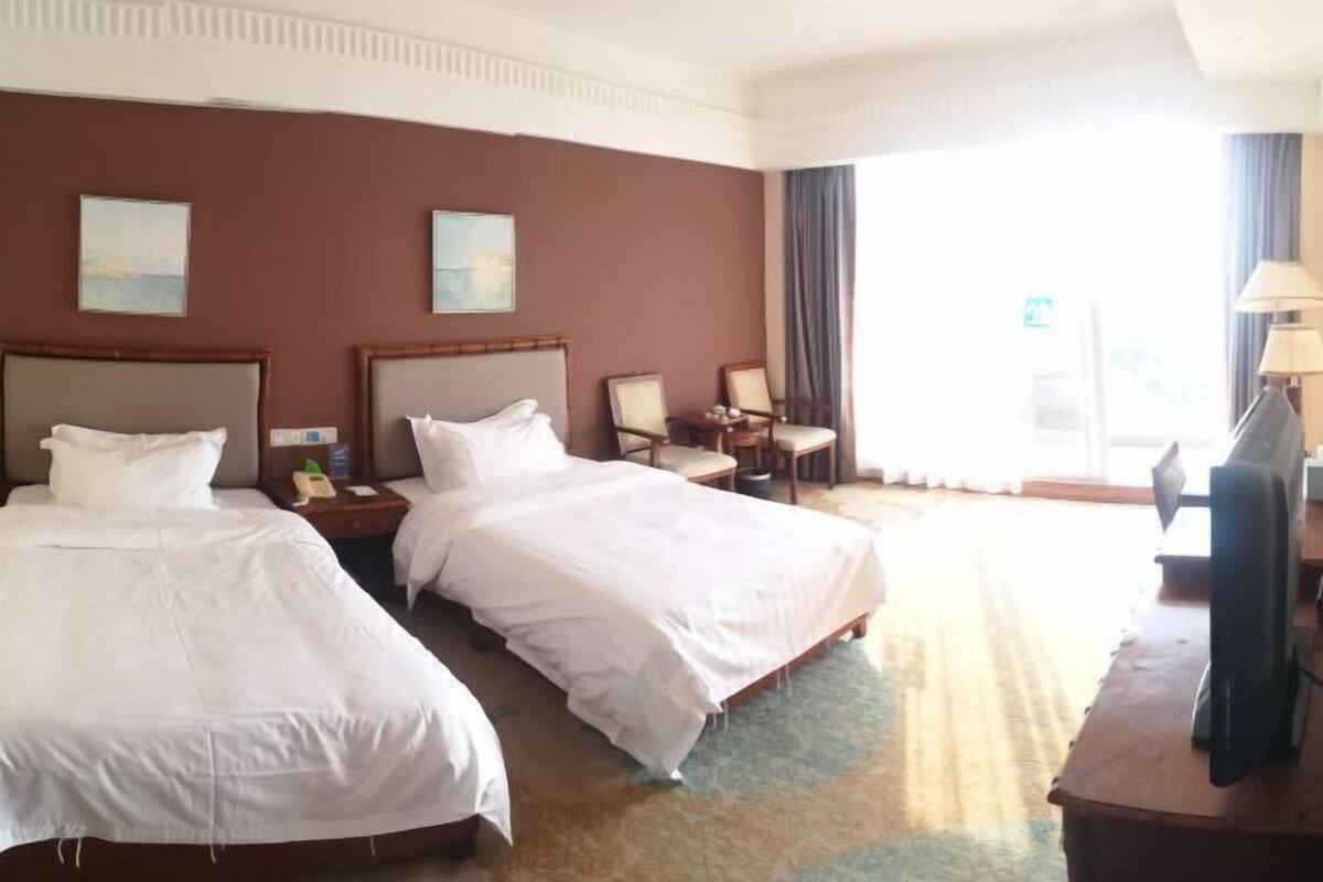 A hotel room with two beds, a desk with a lamp, a chair, and a television.