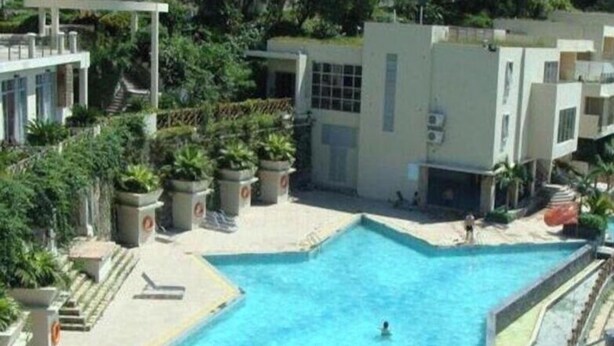 A swimming pool surrounded by buildings, with steps leading to a covered area. - Shell BAY Resort (Shenzhen)