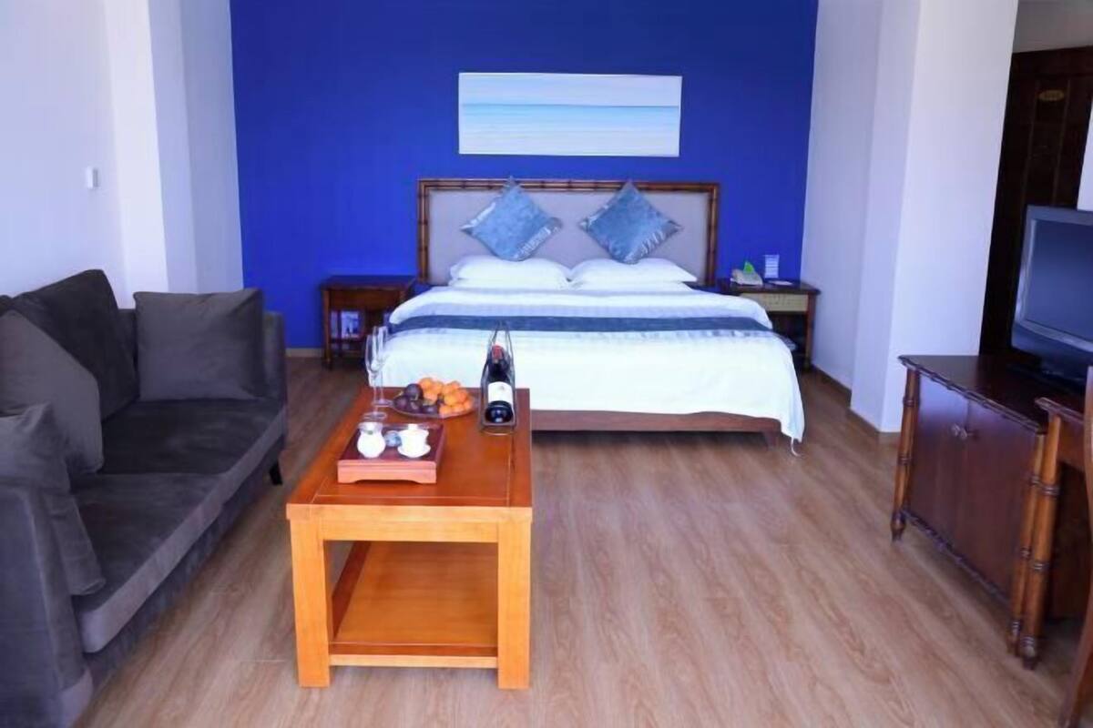 A bedroom with a bed, a TV, a coffee table with fruits and a bottle, and a sofa.