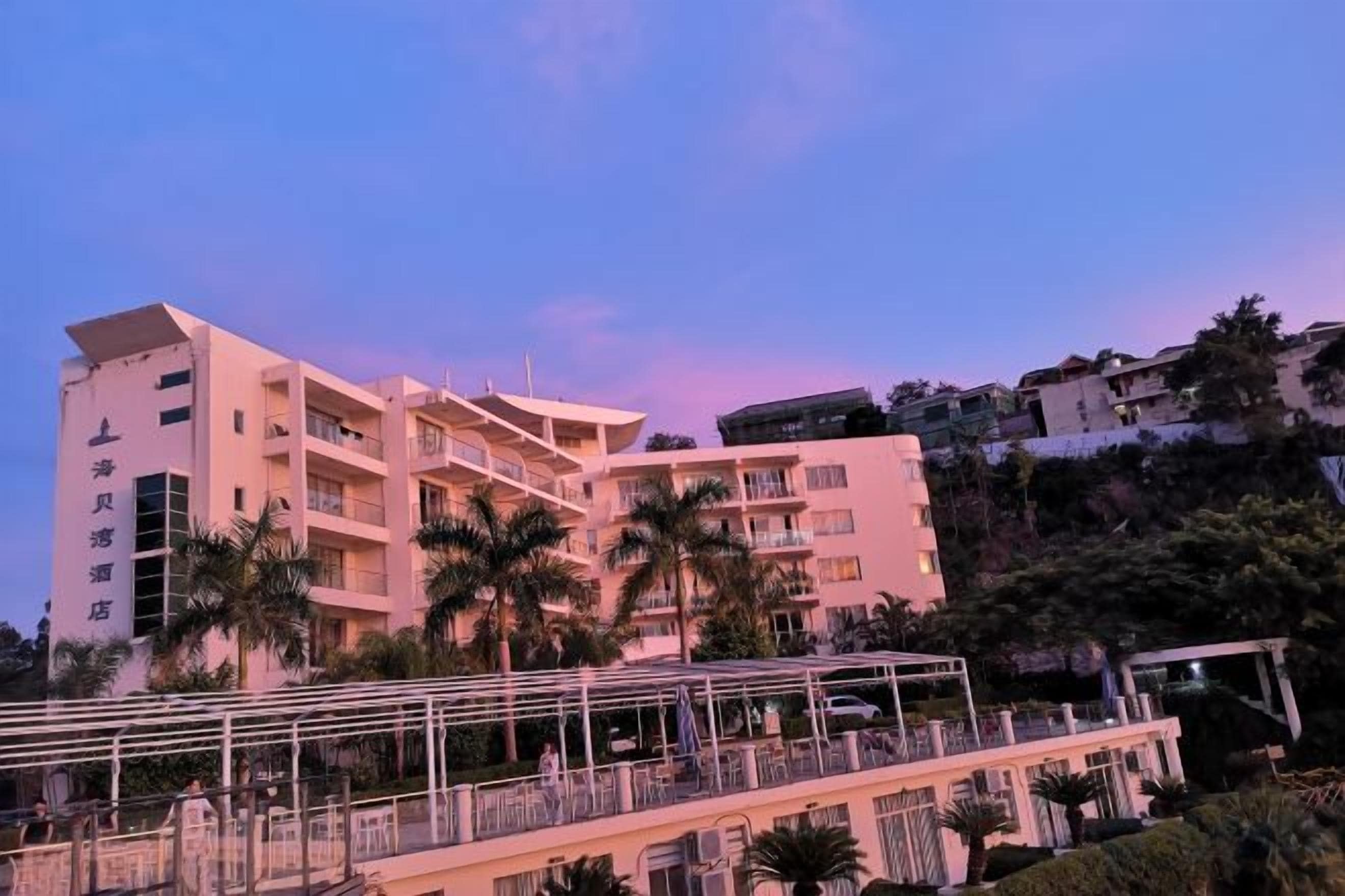 Ein mehrstöckiges Hotel mit Balkonen, Palmen und blauem Himmel.