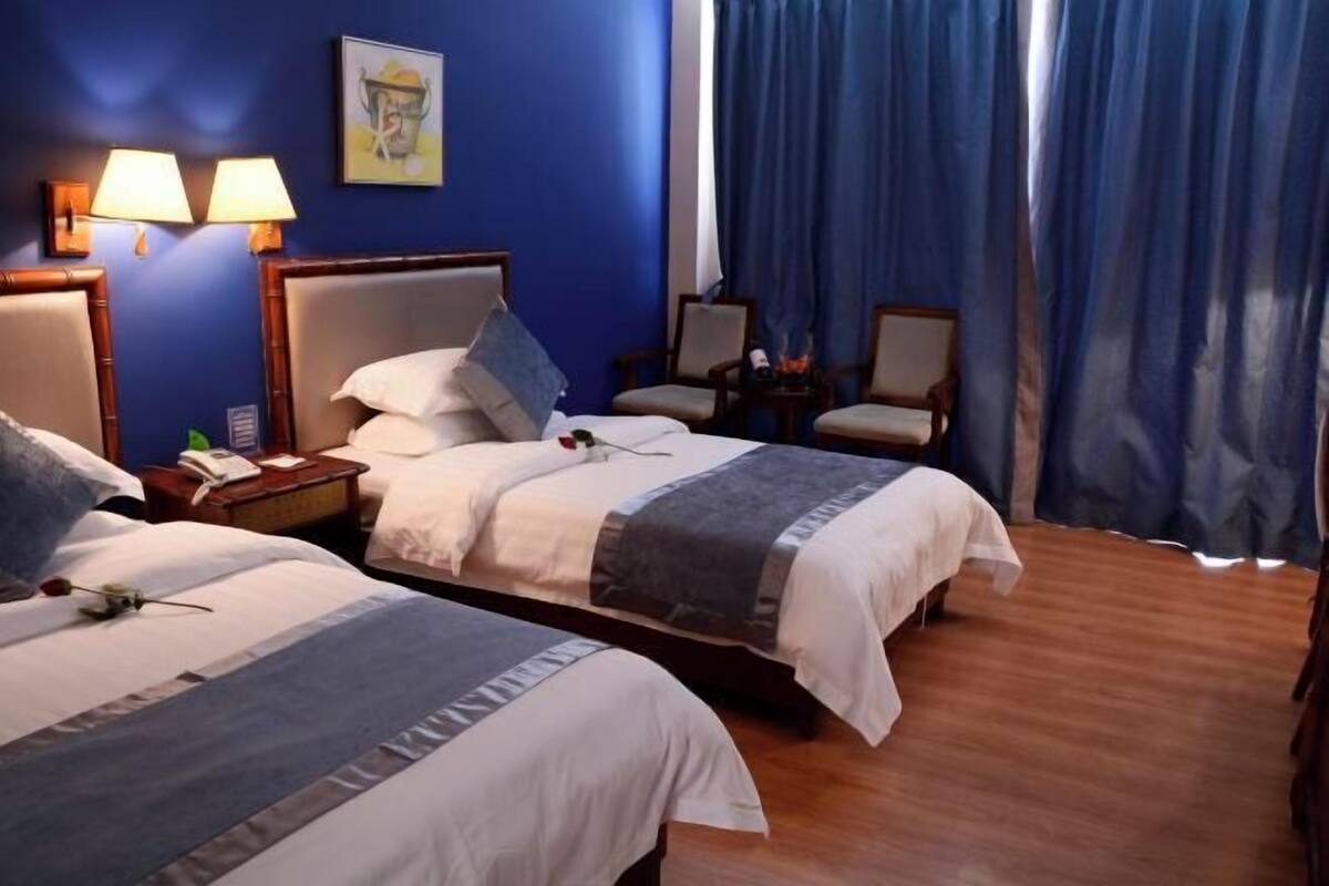 A hotel room with two beds, a nightstand with a lamp, a chair, and a window with curtains.